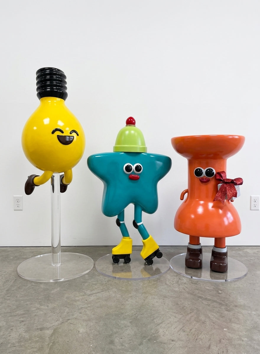 Three large custom character sculptures, a smiling yellow lightbulb, a teal star on roller skates, and an orange figure holding a gift, each mounted on a clear acrylic base
