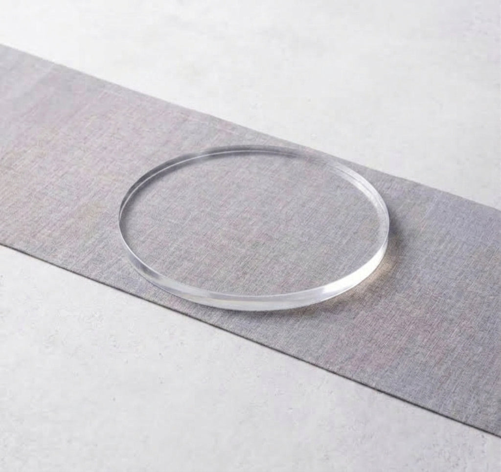 A clear, transparent circular acrylic or glass ring resting on a diagonal gray textured strip against a light gray background.