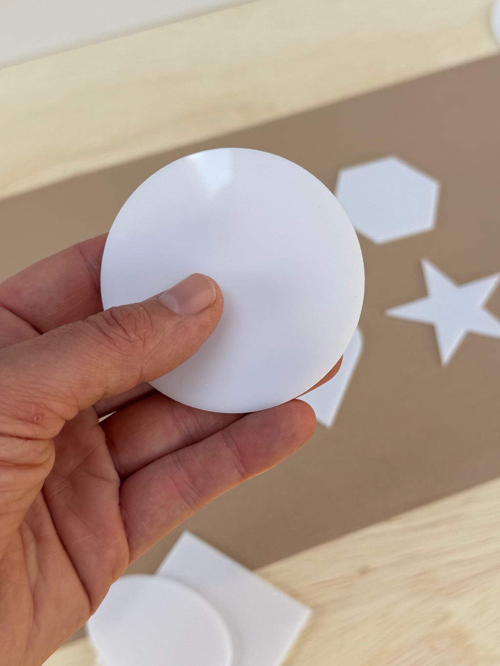 White 1/8 inch acrylic circle blank for UV printing held in hand to show size