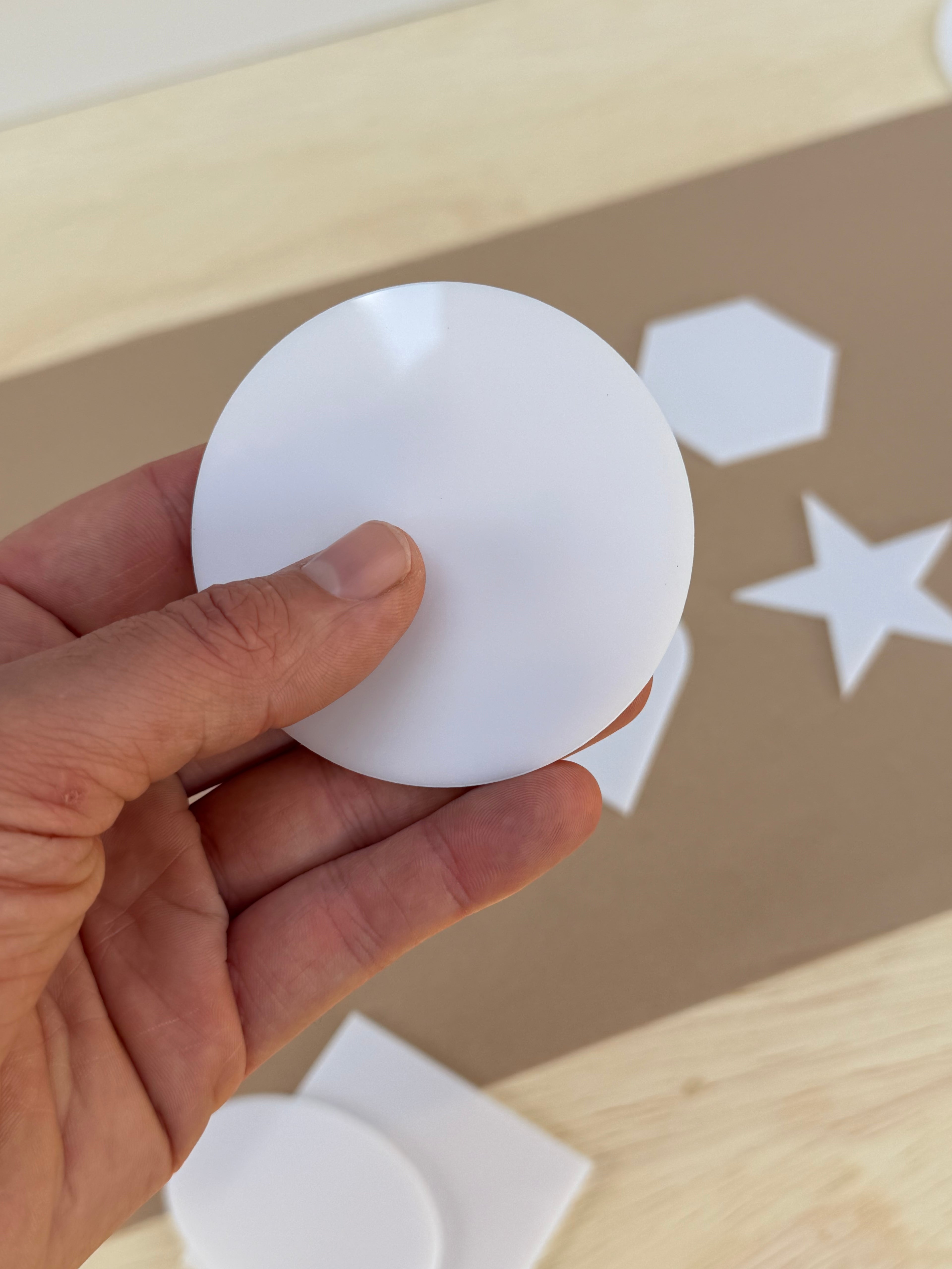 White 1/8 inch acrylic circle blank for UV printing held in hand to show size