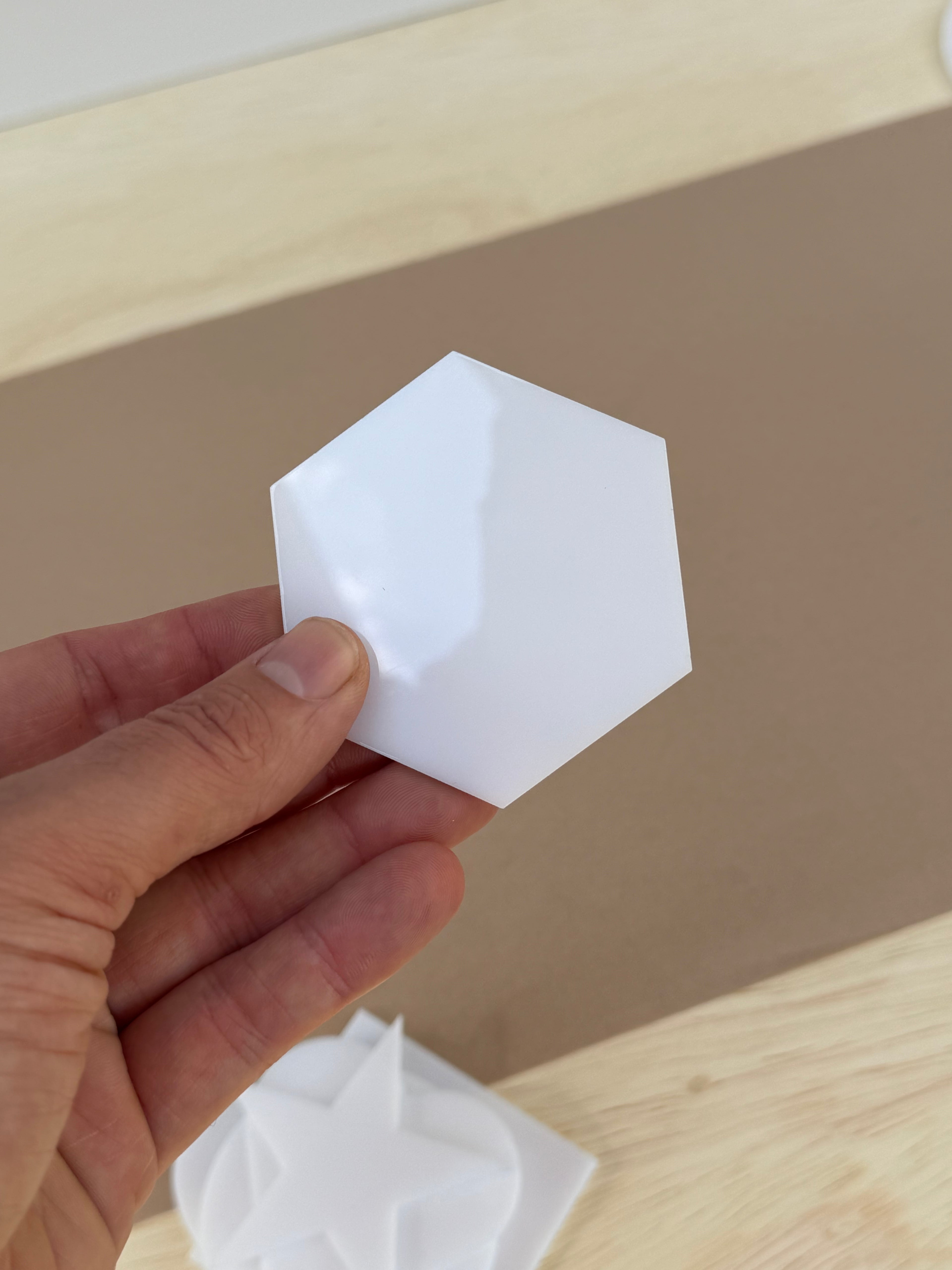 White 1/8 inch acrylic hexagon blank for UV printing held in hand to show size