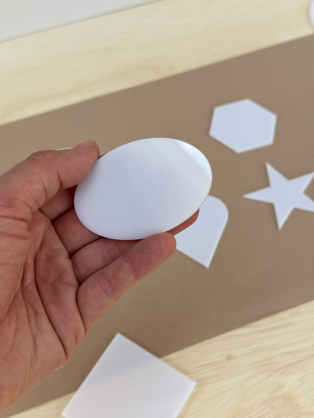 White 1/8 inch acrylic oval blank for UV printing held in hand to show size